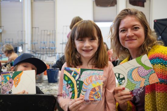 A woman with her son and daughter holding up colorful zentangle drawings in an art studio